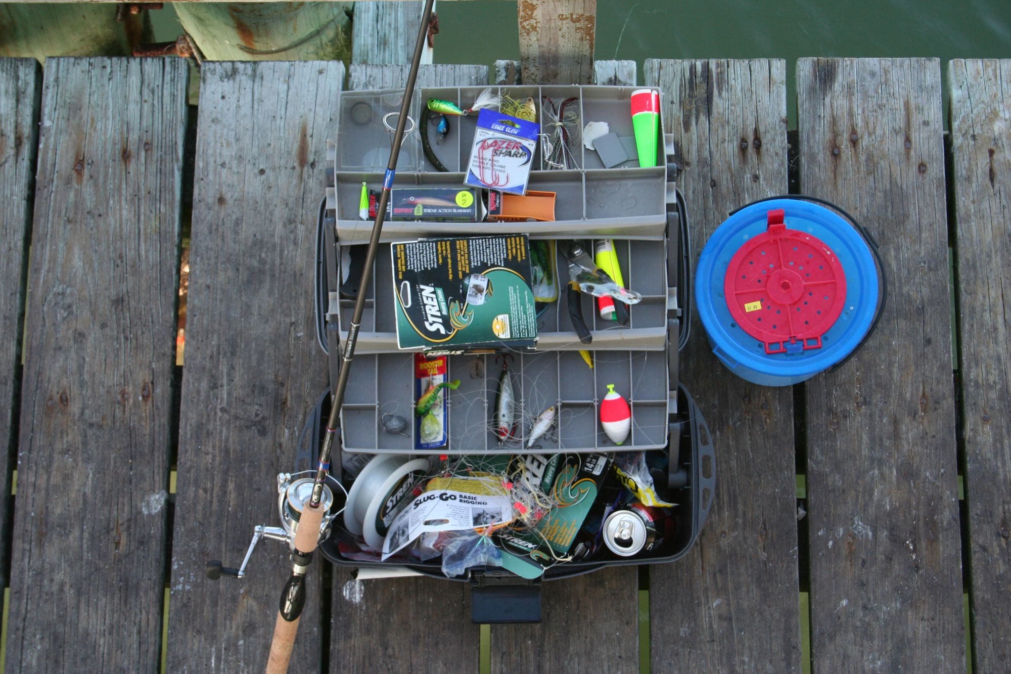 A tackle box, fishing rod, and bait bucket set up on a pier