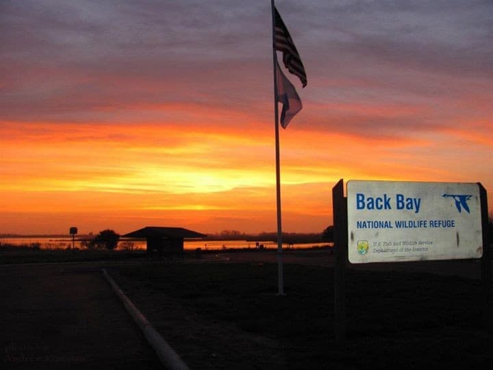 Sunset over the water at the Back Bay National Wildlife Refuge entrance, with the refuge's own sign visible